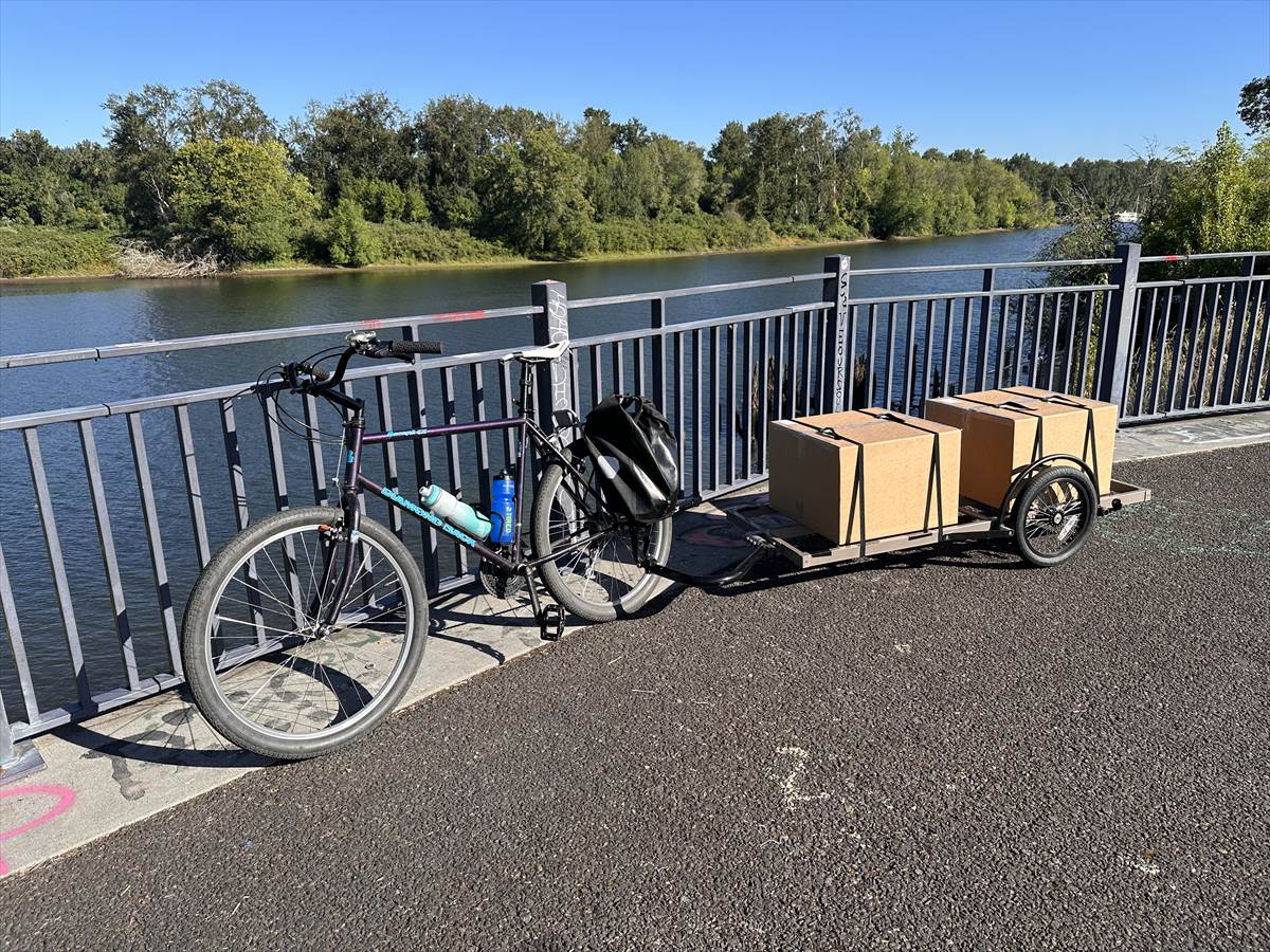 A bicycle and cargo trailer loaded with two boxes on a riverside path in Portland