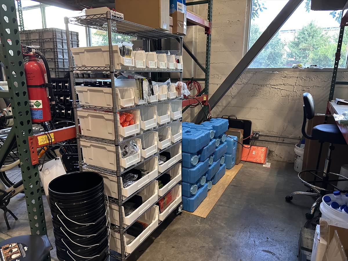 Shelves of sorted kit components and stacked water containers at the PDX Quake Prep warehouse in inner Southeast Portland